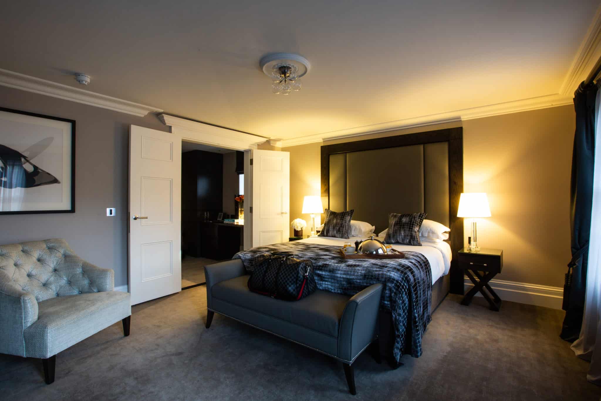 Bedroom at one Warwick park with a suitcase on a bench and a tray with food and coffee on the bed