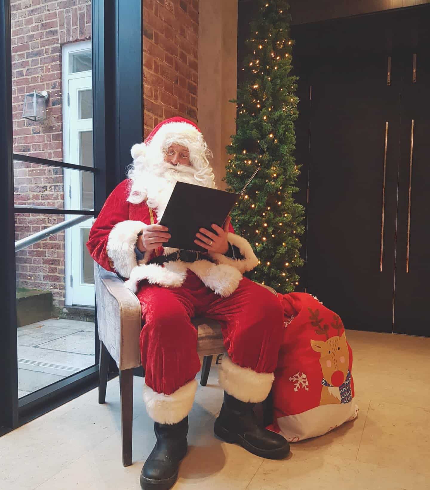 a father christmas sits in a chair next to a christmas tree in One Warwick Park Hotel