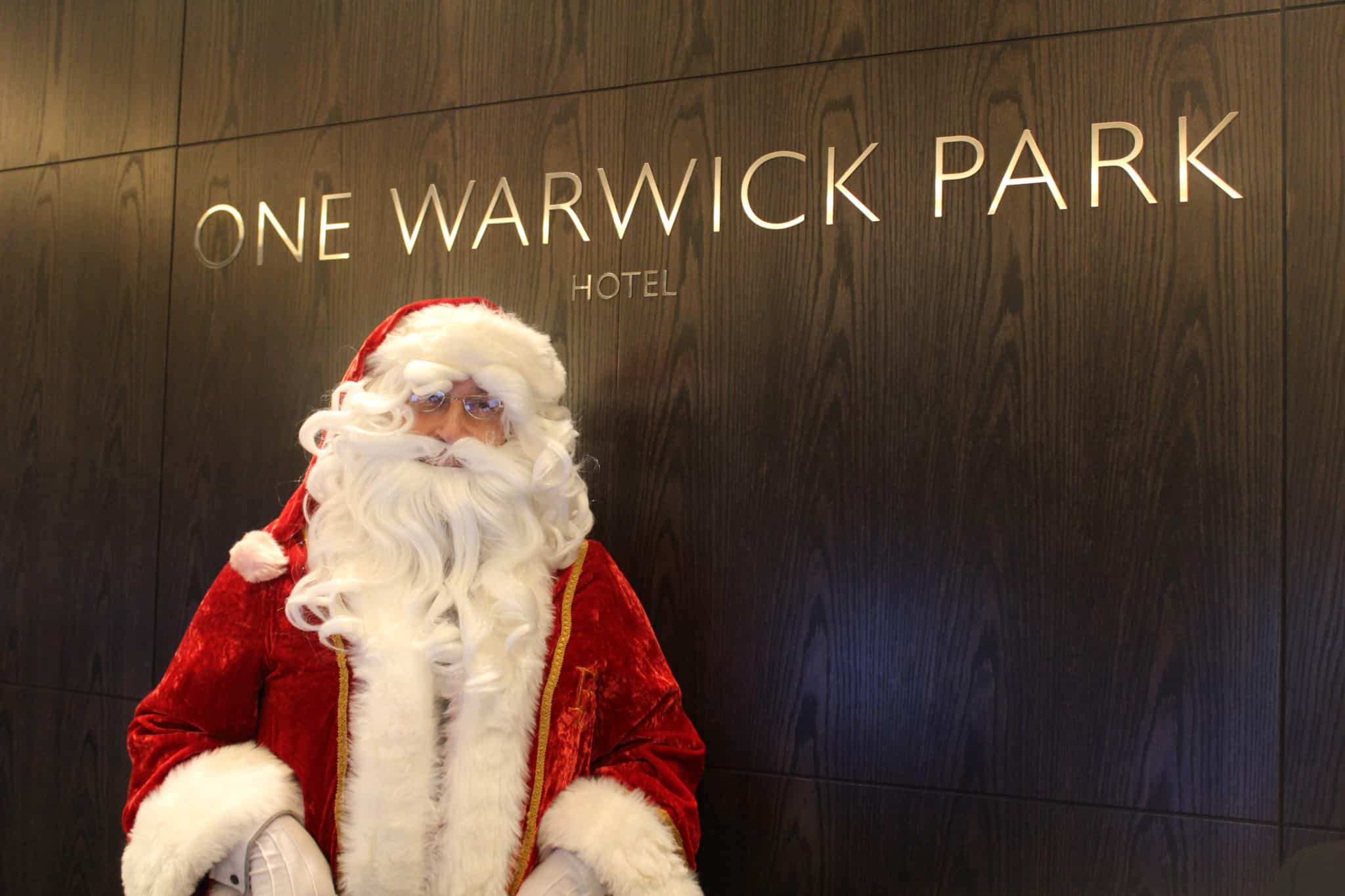 Man dressed as Santa Claus standing in front of a wall with One Warwick Park Hotel written on it