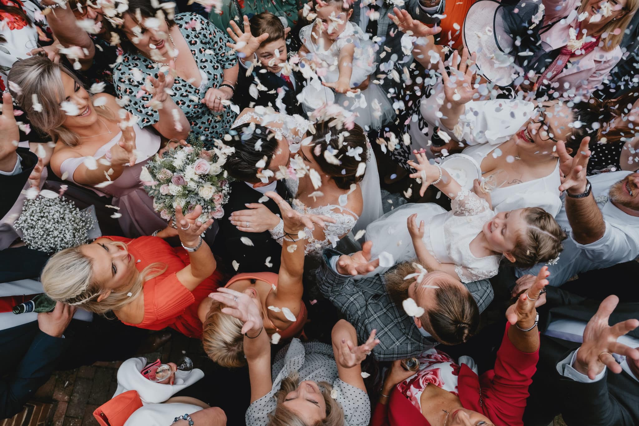 People surrounding a newly wed couple that are kissing under the confetti