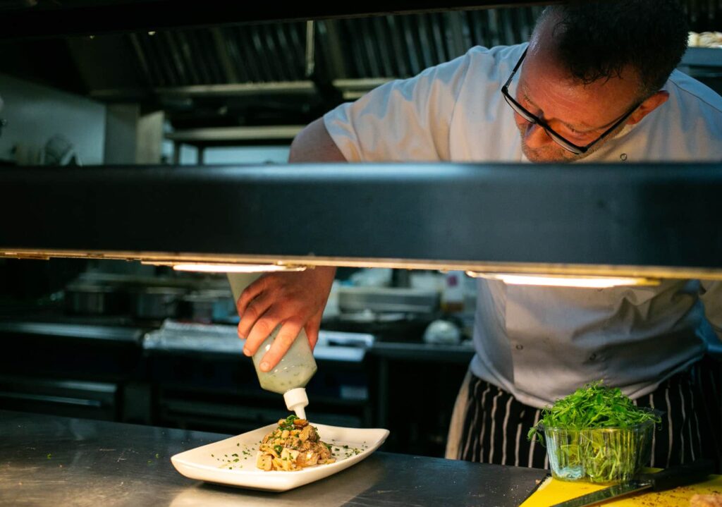 Chef at One Warwick Park Hotel plating a gourmet dish in a professional kitchen during wine tasting evening in Tunbridge Wells preparation.