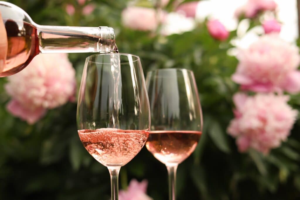 Rosé wine being poured into a glass outdoors with pink peonies in bloom – perfect summer wine tasting evening in Tunbridge Wells setting.