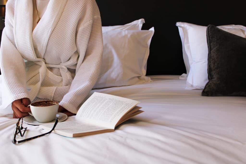 Guest relaxing at a luxury hotel in Tunbridge Wells with coffee and a book on a crisp white bed at One Warwick Park Hotel.