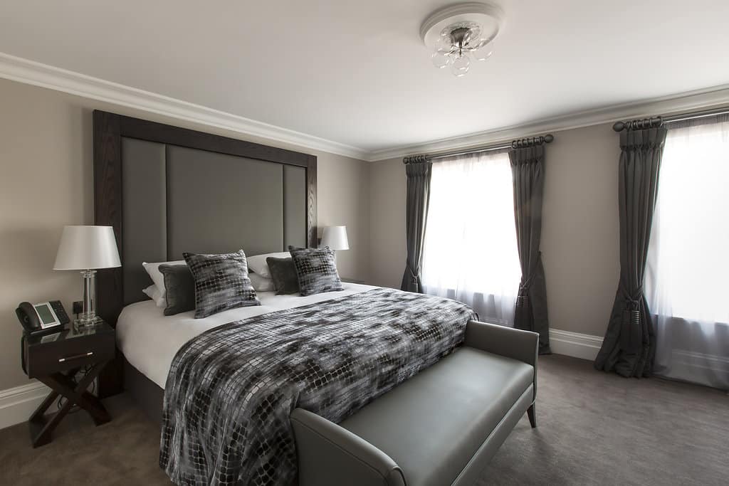 Luxury hotel bedroom with king-size bed, elegant grey décor, and natural light from large windows – perfect for a Kent getaway in Tunbridge Wells