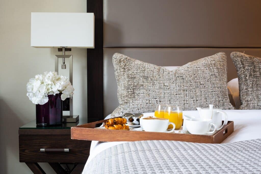 A stylish hotel bedroom in Royal Tunbridge Wells with a breakfast tray on the bed, featuring pastries, coffee and juice – promoting comfort and luxury for Black Friday hotel deals.