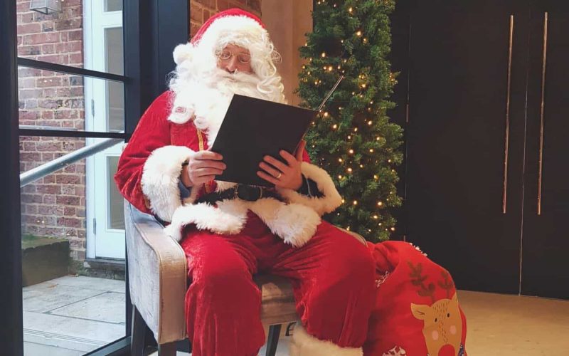 a father christmas sits in a chair next to a christmas tree in One Warwick Park Hotel